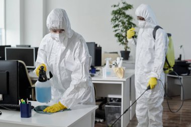 Contemporary disinfection service company staff in protective workwear carrying out their work in spacious openspace office clipart