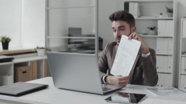 Akşamüstü masasında beyaz renkli bir ofiste oturan mavi gözlü beyaz işadamı portatif bilgisayardan video çağrısında bulundu ve web kamerasındaki belgeleri gösterdi.