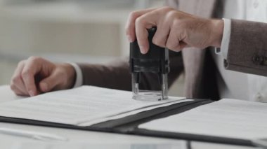 Midsection of two cropped men sitting at desk in office at daytime, putting stamp on document, then shaking hands