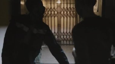 Handheld of young Caucasian woman with shaved head holding shotgun, running away from zombies in creepy old building