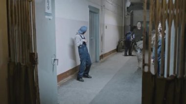 Locked down of young Caucasian woman with shaved head running away, shooting zombies, escaping behind old elevator gate in creepy dark building