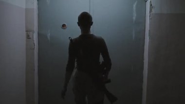 Kafası tıraşlı bir askeri kadının, karanlık, ürkütücü bir binada yürümesi, kapıları açması, eski asansörün metal kapısının arkasında sıkışmış üç zombiye bakması.