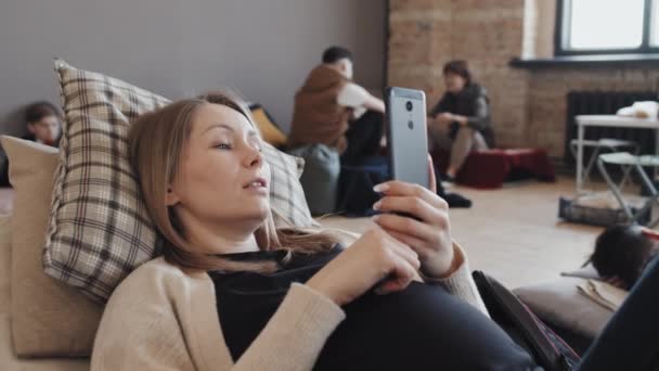 中くらいのブロンド白人妊娠中の女性スマートフォンを使用して 昼間の避難所でベッドの上に横たわっビデオ通話 — ストック動画