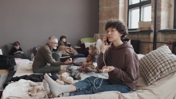 许多白种人年轻的卷曲女子坐在难民庇护所地板上的床垫上 白天在手机上和其他难民交谈 — 图库视频影像