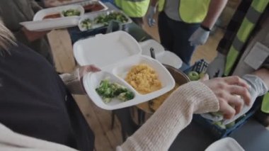 Yeşil yelekli yüksek açılı gönüllülerin ihtiyacı olan insanlara sağlıklı bir akşam yemeği ve gündüz barınağında taze elmalar sağlaması