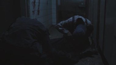 Low angle of two zombies feeding on dead body, then spotting and following female soldier with shaved head holding flashlight, inspecting dark and creepy abandoned building
