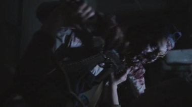 Medium long low angle of woman with shaved head lying on floor in dark public bathroom with lights twitching, defending against living dead, pushing zombie away with shotgun