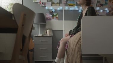 Tilting up of young bored Caucasian female adult with nasal cannula sitting on bed in decorated hospital ward, moving legs in air