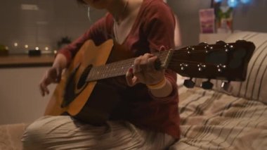 Midsection of Caucasian teenage girl with nasal cannula sitting on bed in hospital room decorated with garlands at night, playing acoustic guitar and singing