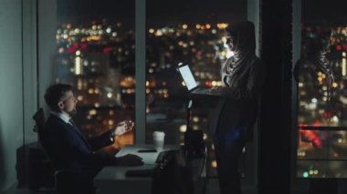 İslami başörtüsü takmış, elinde laptopla karanlık bir ofiste beyaz erkek meslektaşından gecenin geç saatlerinde sunum için tavsiye isterken tam bir Müslüman kadın ofis çalışanı.