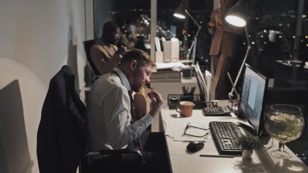 3名男性和女性多族裔办公室工作人员深夜坐在电脑前的办公桌前 用筷子吃外卖面 背景为城市灯火通明 — 图库视频影像