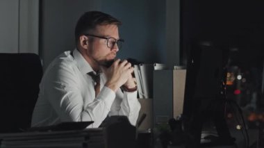 Beyaz gömlekli ve kravatlı beyaz iş adamının orta boy portresi. Geceleri ofiste tek başına oturuyor, ekranda belge okuyor, sonra gözlüğünü çıkarıyor ve yorgun gözlerle kameraya bakıyor.