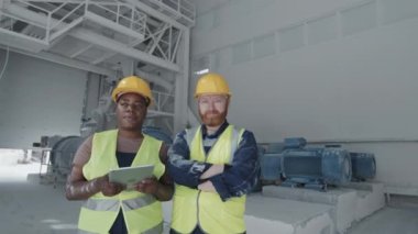 African American and Caucasian marble factory workers standing against ball mill machines looking at camera