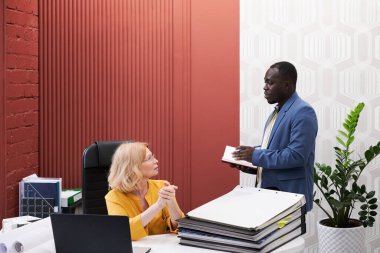African businessman talking to manager and making notes in notebook during their conversation at office