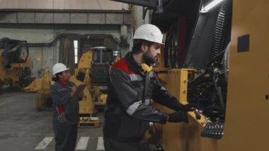 Medium side view of male Caucasian factory worker in hard hat and uniform fixing machinery at plant