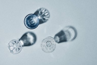 Flatlay of three glasses containing transparent pure water on grey background surrounded by copyspace for your text