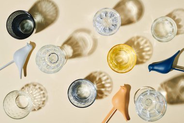 Several glasses containing clean water, their shadows and three plastic birds of blue, white and beige color over pastel background