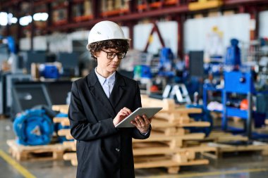 Young female engineer with tablet scrolling through online information about production stages of new equipment produced by factory