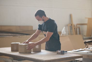 Young man in protective mask preparing packages for shipping, he working at table in warehouse
