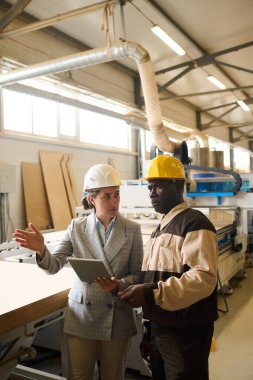 Young businesswoman using digital tablet and discussing working process with foreman at factory