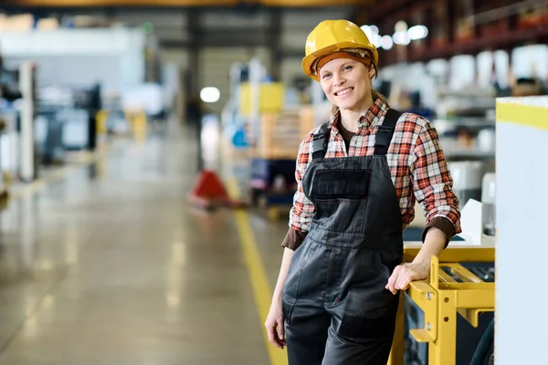 Successful technical inspector or manager of large factory looking at camera with smile while standing by industrial equipment