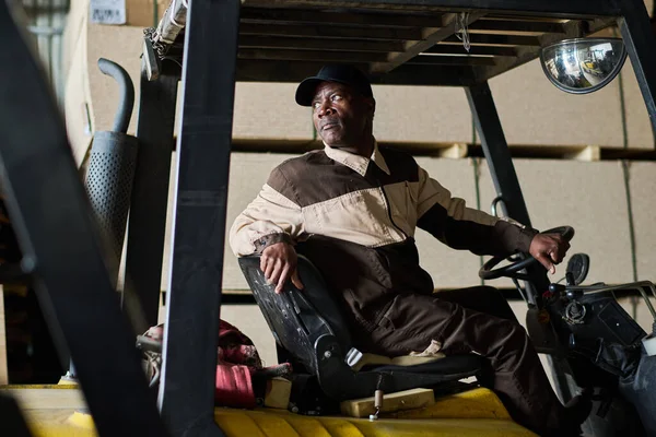 身穿制服的非洲男性工人在仓库驾驶叉车和运输货物 — 图库照片