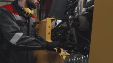 Tilting up of male Caucasian factory worker in hard hat and uniform fixing machinery at plant