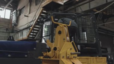 Wide of African American female technician in orange hard hat and work overalls sitting inside cabin of new machinery at factory, inspecting it, using tablet