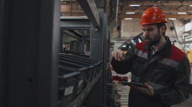 Medium of male Caucasian quality control worker checking parts in boxes at factory, using tablet computer