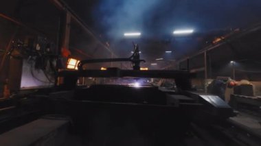 Drone tracking view of automated equipment producing metal parts at dark factory, people working around