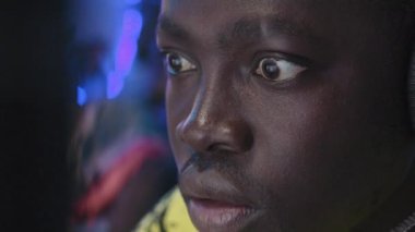 Video oyunu oynarken ve mikrofona konuşurken, kulaklık takmış, bilgisayar ekranına bakan genç siyahi erkek oyuncunun yüzünün ve gözlerinin şok görüntüsü.