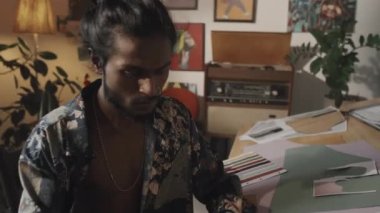 Indian fashion designer using liquid glue while making inspirational mood board, sitting at wooden worktable in creative messy workshop
