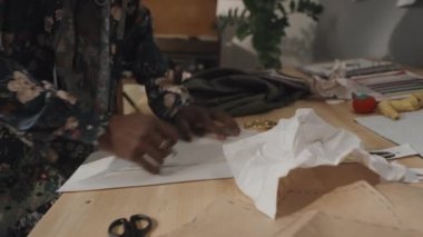 Emotional young male Indian fashion designer making sketch on crumpled piece of paper in messy workshop