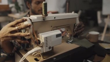 Stylish Indian designer using sewing machine while manufacturing clothes in creative workshop