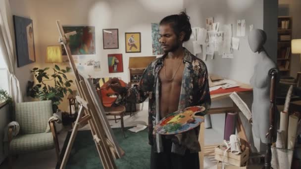 Medium Portrait Handsome Indian Artist Holding Artist Palette Standing Canvas — стоковое видео