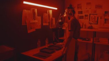 Medium shot of concentrated young male Indian photographer developing photographic paper in darkroom