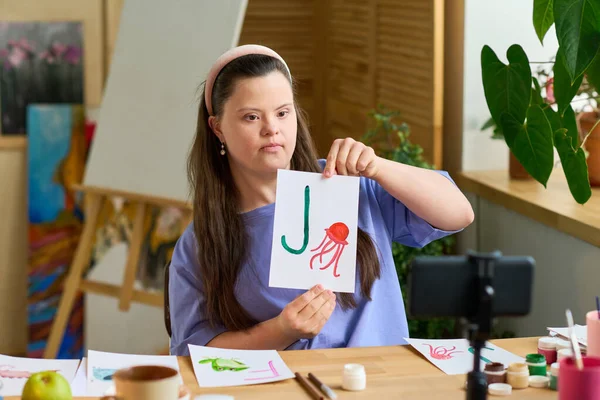 患有唐氏综合症的女孩坐在摄像机前 一边用英文字母展示纸 一边在网上吸引水母 — 图库照片