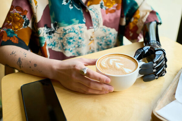 Hands of young woman with partial arm holding cup of cappuccino with fluffy milk foam and creative spiral heart shaped decor