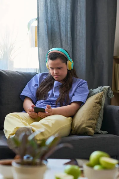 坐在舒适的沙发上看着智能手机屏幕的患有唐氏综合症的年轻女性 — 图库照片
