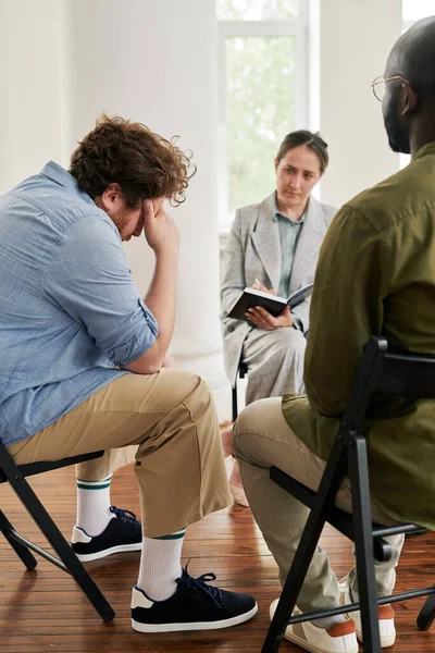 一位肥胖的年轻人坐在心理医生面前 一边摸着自己的头 一边和其他病人一起向她描述他的问题 — 图库照片