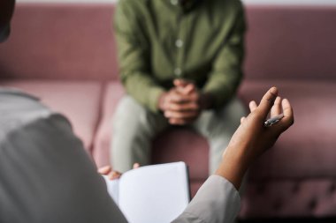 Genç Afrikalı Amerikalı psikanalist, seans sırasında önünde oturan erkek hastasına tavsiye veriyor.