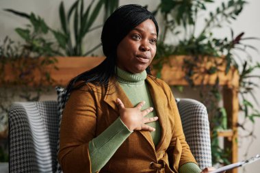 Hasta sorunlarını tartışırken ve seansta tavsiye verirken kendine güvenen genç bir kadın psikolog elini göğsüne koyuyor.