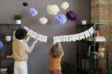 Doğumgünü partisine hazırlanmak için oğluyla birlikte poster asan genç annenin dikiz görüntüsü.