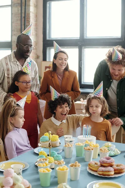 デザートとテーブルに座っている間 誕生日ケーキの上にろうそくを吹いてパーティーの帽子の小さな男の子と大人と子供と誕生日を祝う — ストック写真