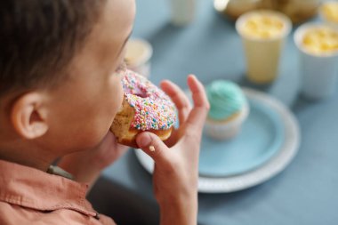 Küçük çocuğun masada otururken jöleli donut yediği yakın plan. Partide tatlının tadını çıkarıyor.