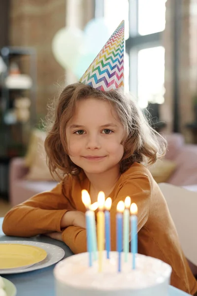 パーティーの帽子で誕生日の男の子の肖像カメラを見ながらテーブルに座っている誕生日ケーキと燃えさかるキャンドル — ストック写真