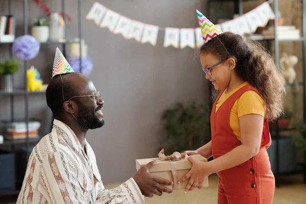 パーティーでアフリカ系アメリカ人の父は彼女にギフトボックスを与える誕生日で彼の娘を祝うために喜んで帽子 — ストック写真