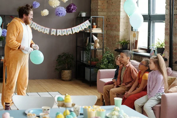 生日宴会上 身穿动物服装的动画师用气球把氦气塞入嘴里 在沙发上用滑稽的声音与孩子们交谈 — 图库照片