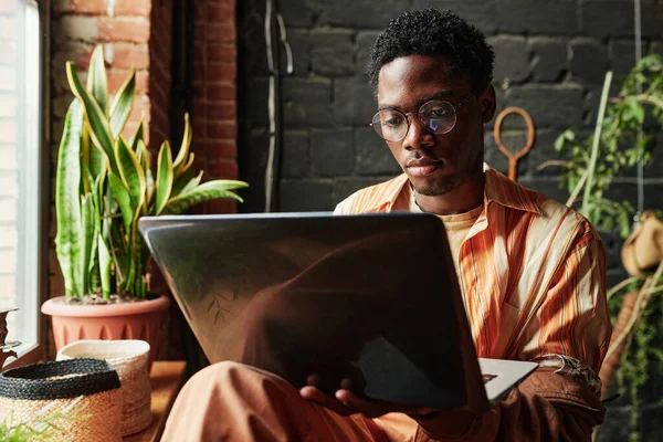 Młody Poważny Czarny Człowiek Casualwear Okulary Pomocą Laptopa Podczas Siedzi — Zdjęcie stockowe