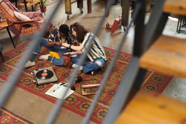 年轻夫妇坐在客厅地板上的红地毯上 讨论着女孩拿着的复古相机屏幕上的图像 — 图库照片